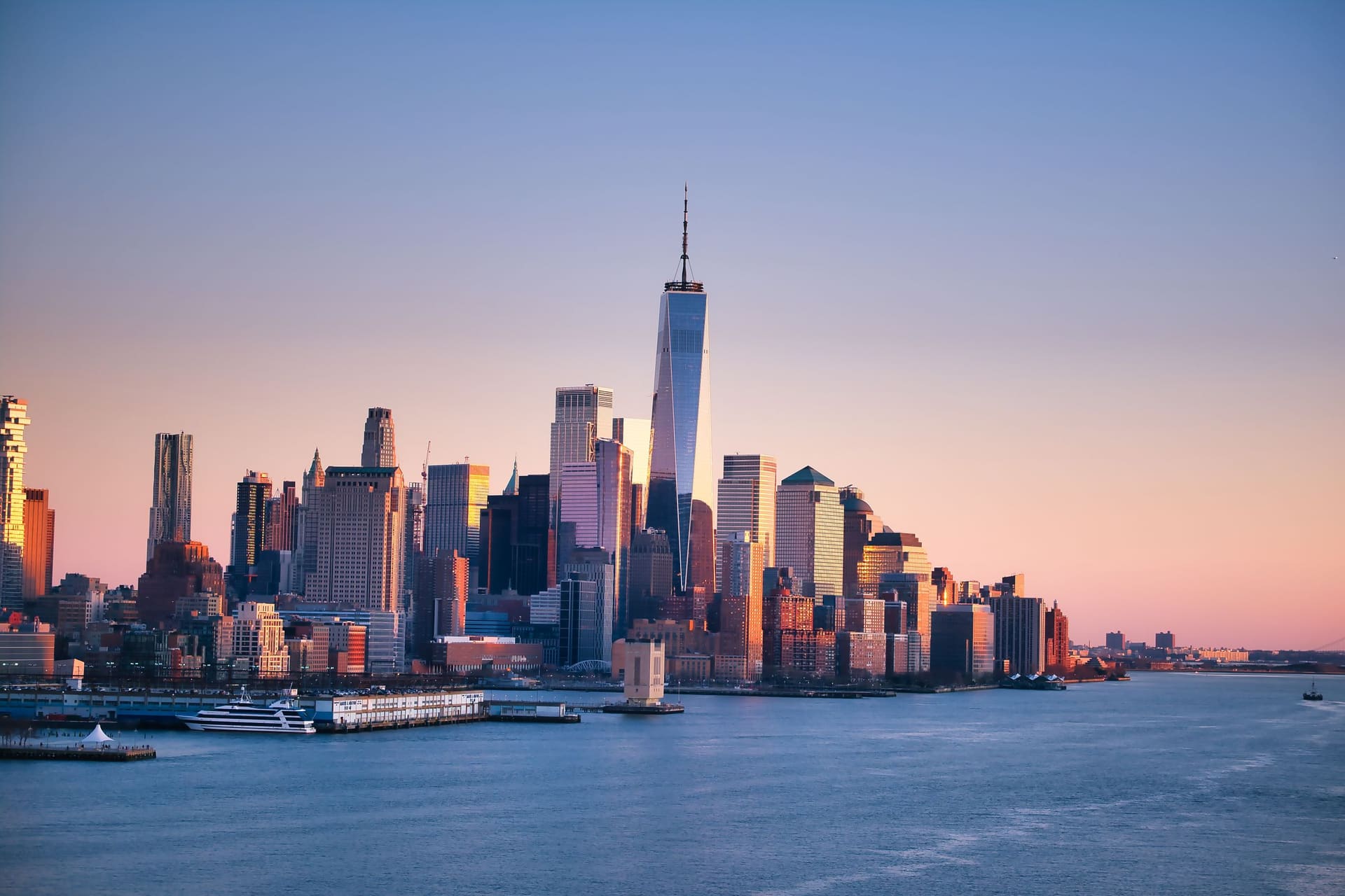 Manhattan skyline across the Hudson River at dusk, with calm water in the foreground